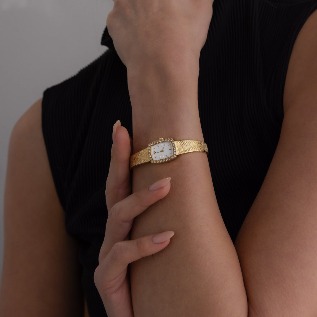 A person wearing a Petite Mesh Timepiece with a gold rectangular face and a black sleeveless top.
