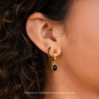 Close-up of a woman's ear with two 18K Gold hoops—one featuring a black stone, the other with green accents. Get inspired for your next pair from the Monthly Earrings Subscription Box.