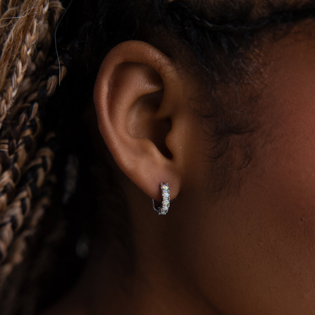 Close-up of an ear wearing a small opal hoop earring with a blurred background