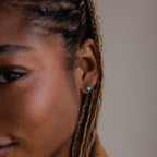 Close-up of a person with braided hair wearing a small silver turquoise stud earring.