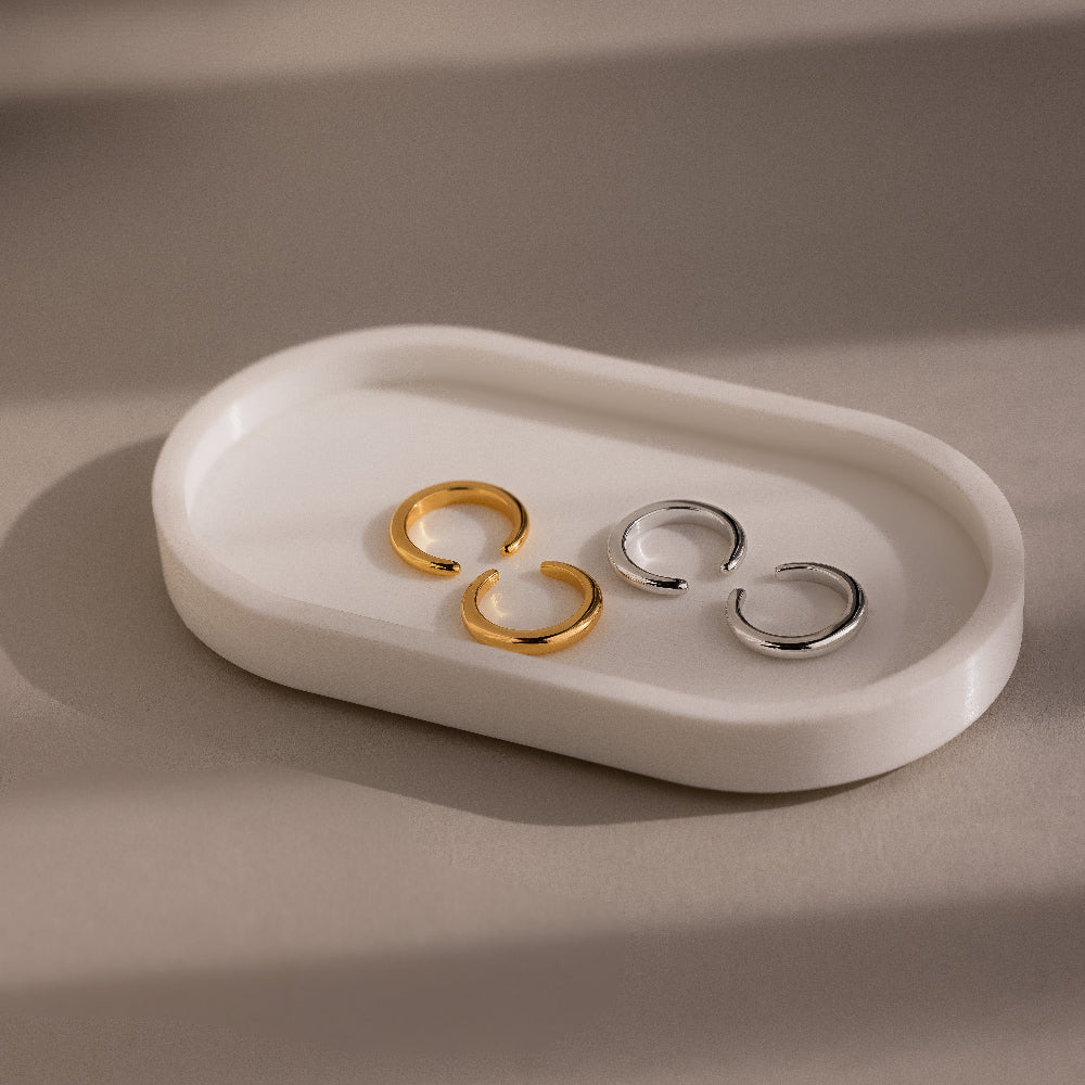Two gold and silver pairs of cuff earrings on a white ceramic dish against a beige background