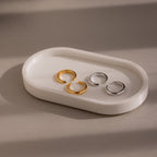Two gold and silver pairs of cuff earrings on a white ceramic dish against a beige background
