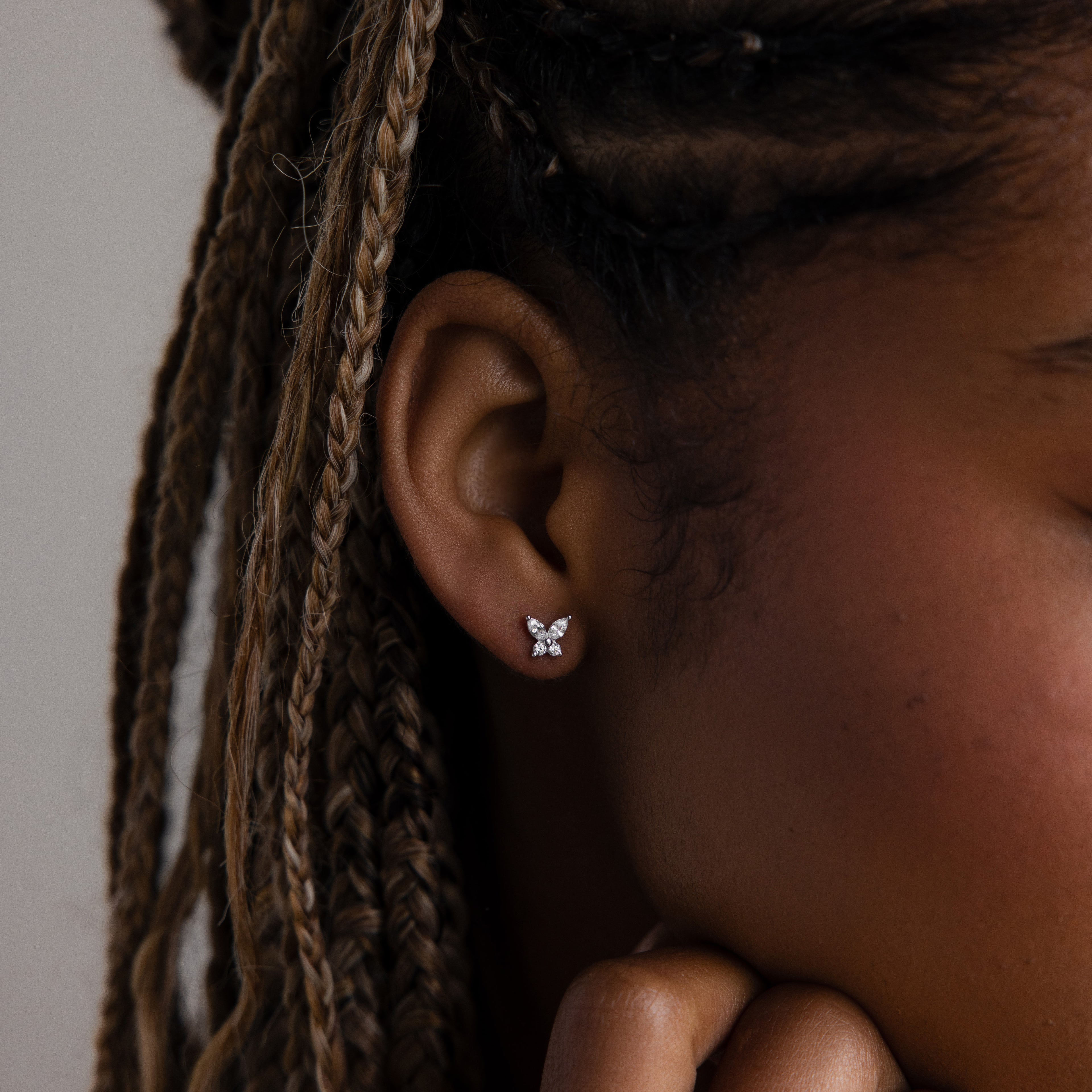 Close-up of an ear with a butterfly-shaped earring against a neutral background