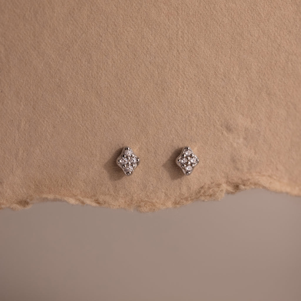 Pair of silver diamond stud earrings on a textured brown surface