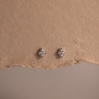Pair of silver diamond stud earrings on a textured brown surface
