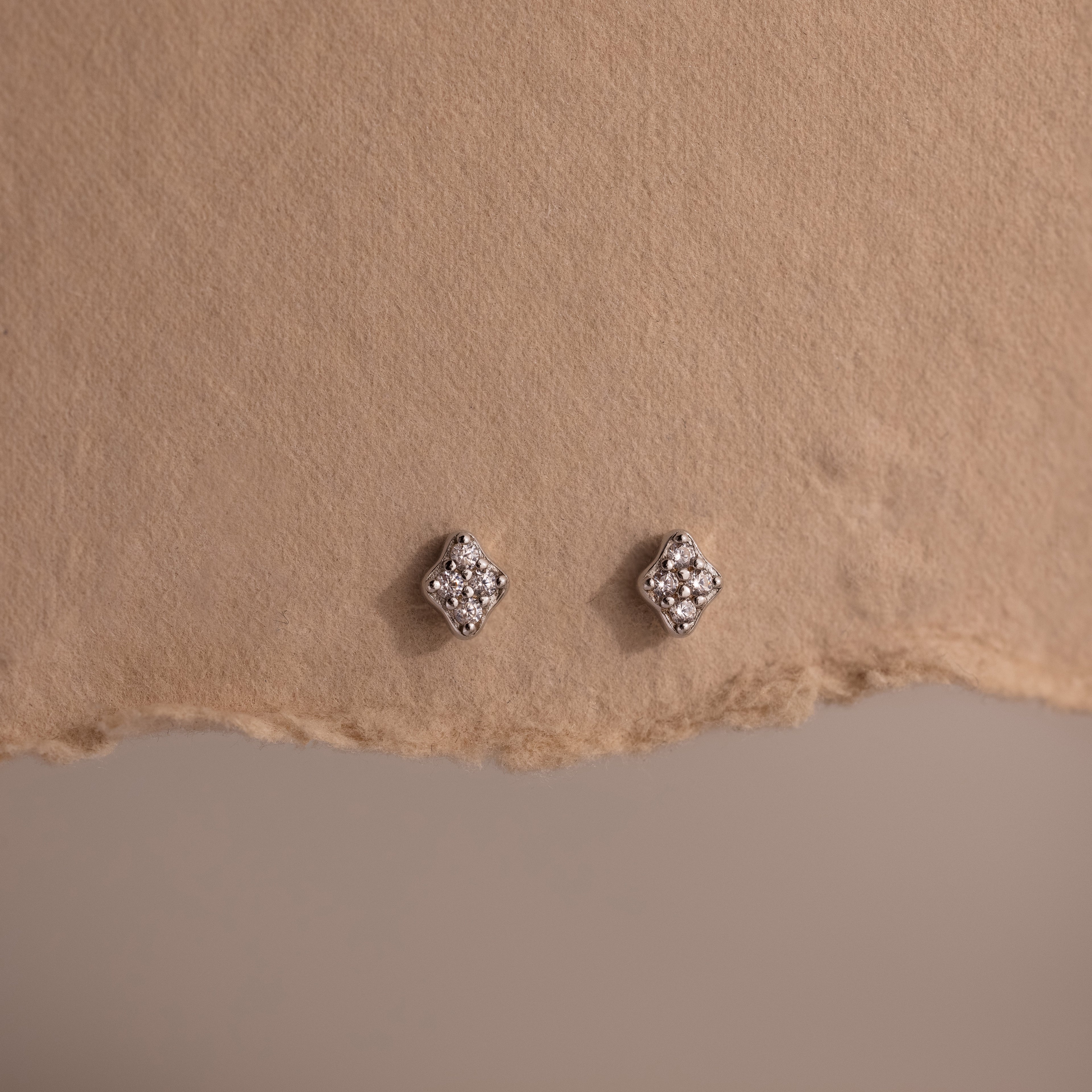 Pair of silver diamond stud earrings on a textured brown surface