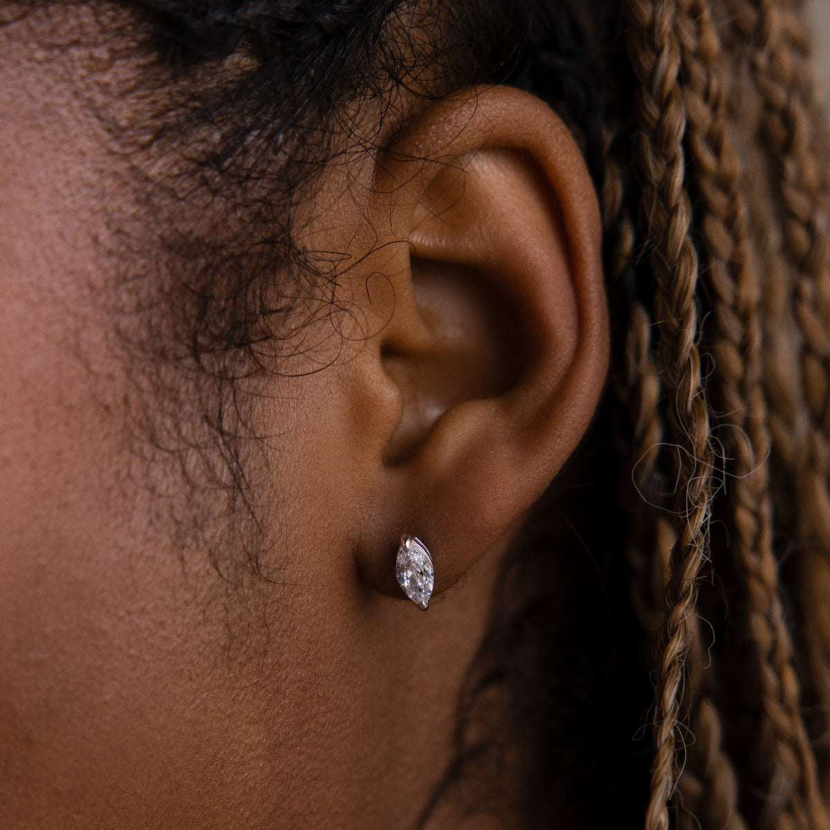Close-up of a model wearing a silver diamond earring with braided hair.