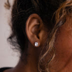 Close-up of a model wearing a silver rectangular diamond earring with blurred background