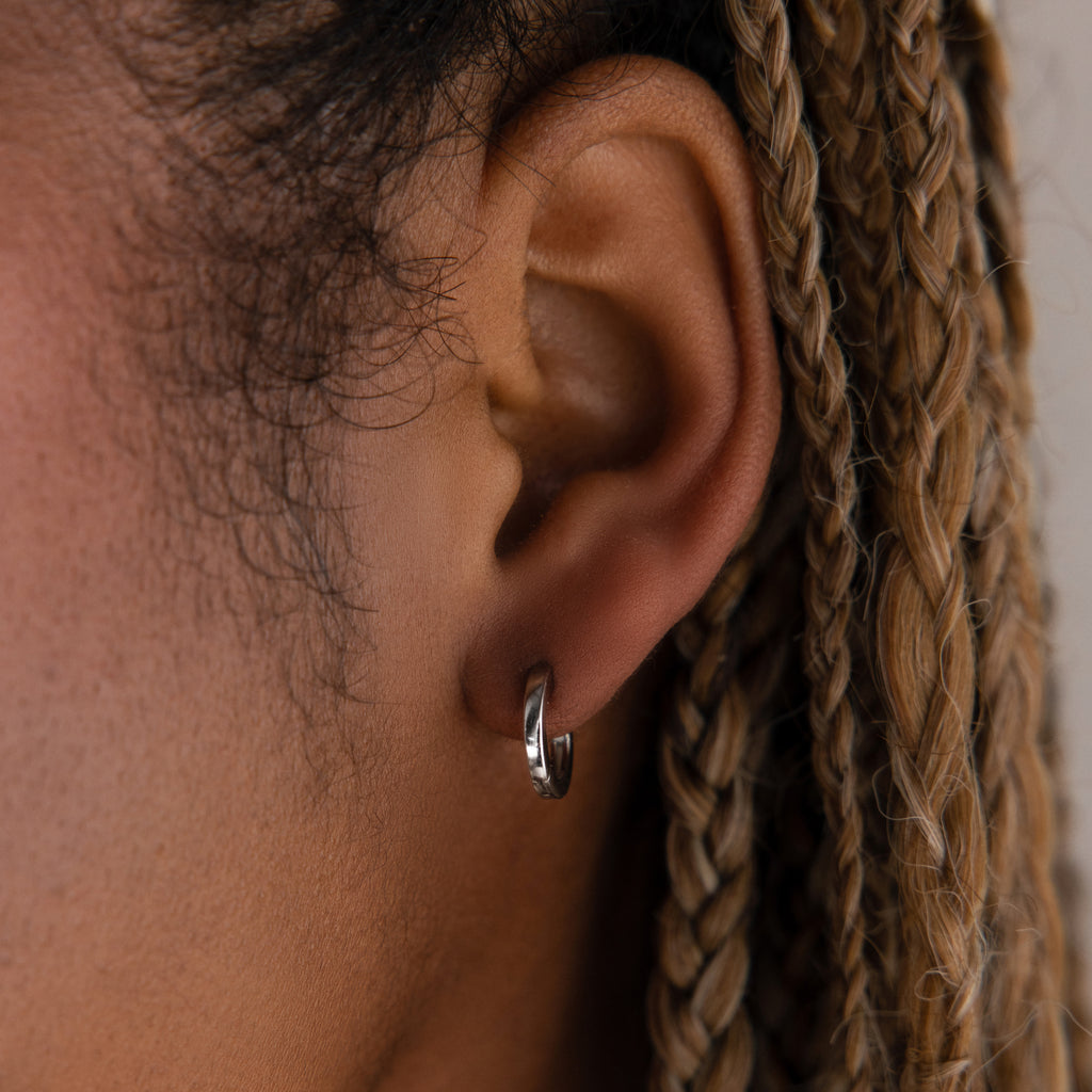 Close-up of a model with a silver huggie hoop earring and braided hair.