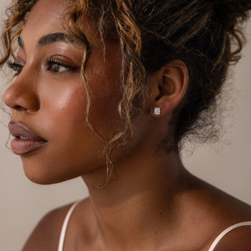 Close-up of a woman wearing silver diamond earrings against a neutral background