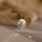 The Bee Coin Necklace features a silver coin pendant with a raised bee design, perfect for layering and shown on a soft beige background.