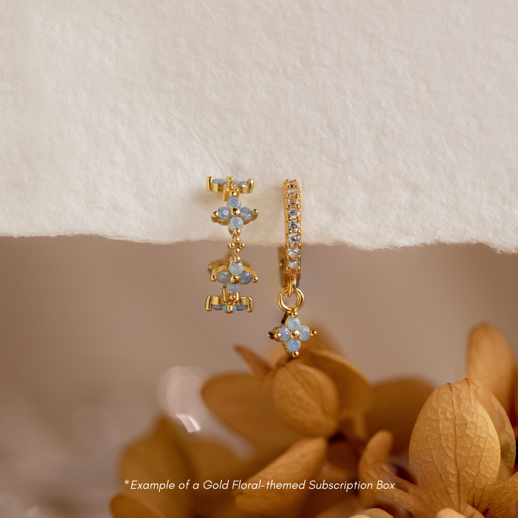 Discover new gold floral 18K earrings each month with our Monthly Earrings Subscription Box, beautifully presented against dried flowers and a cream background.