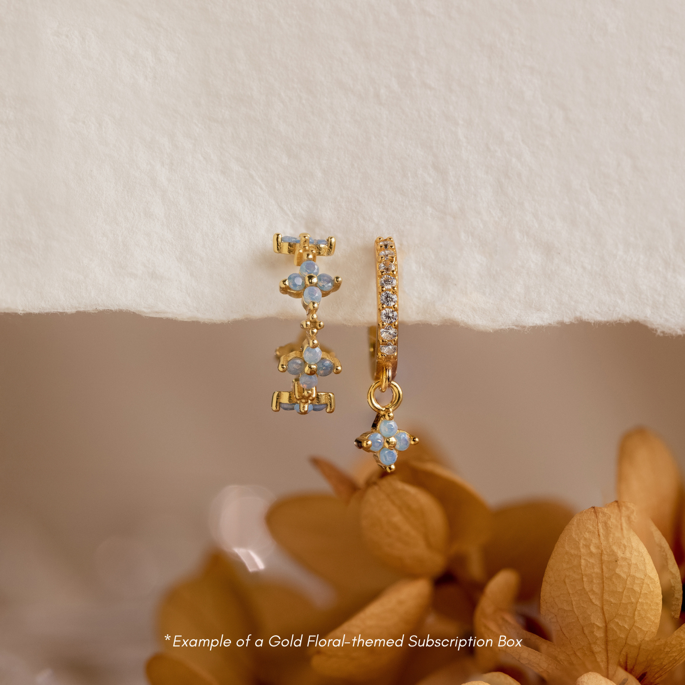 Discover new gold floral 18K earrings each month with our Monthly Earrings Subscription Box, beautifully presented against dried flowers and a cream background.