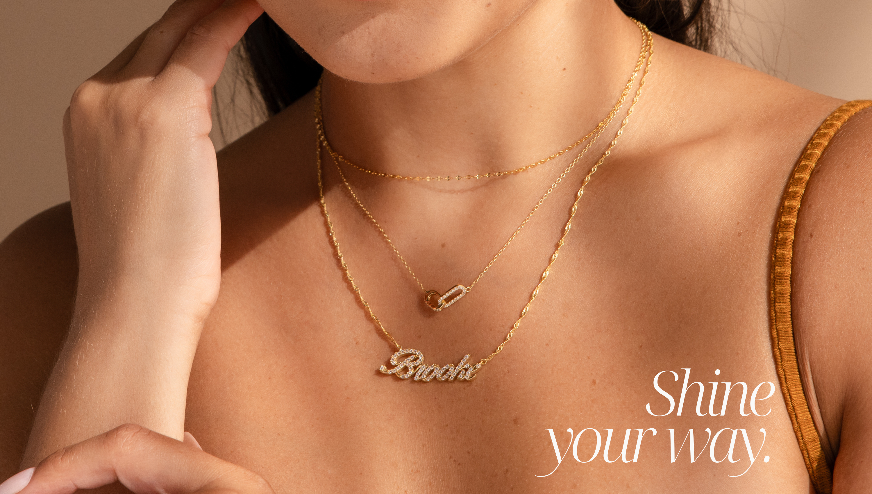 Landscape banner features the text "shine your way" and a brunette model wearing a gold necklace stack consisting of a mirror chain necklace, a pave diamond linked pendant necklace, and a custom pave script name necklace with the name "Brooke" in a twisted chain.