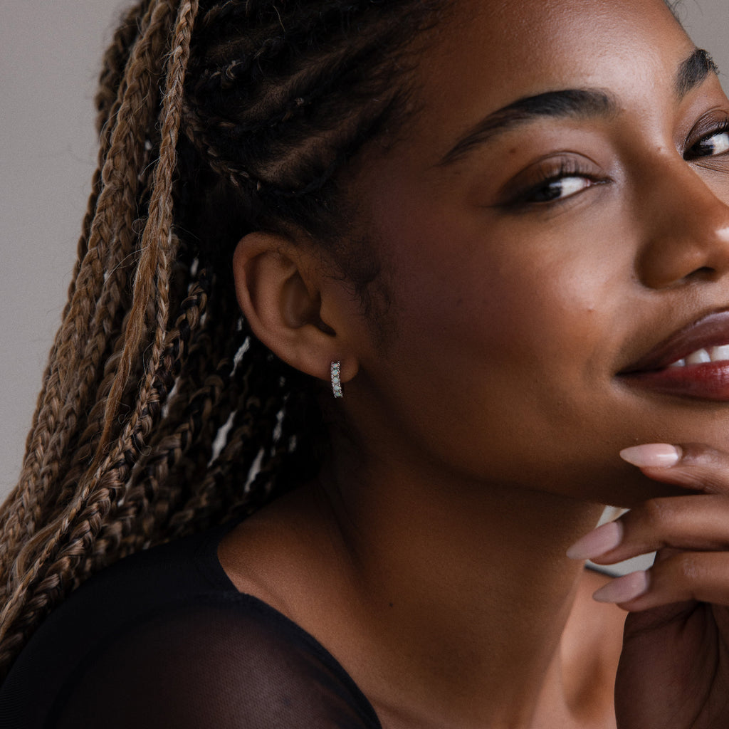 Close-up of a woman with braided hair and silver opal hoop earrings, wearing a black top.