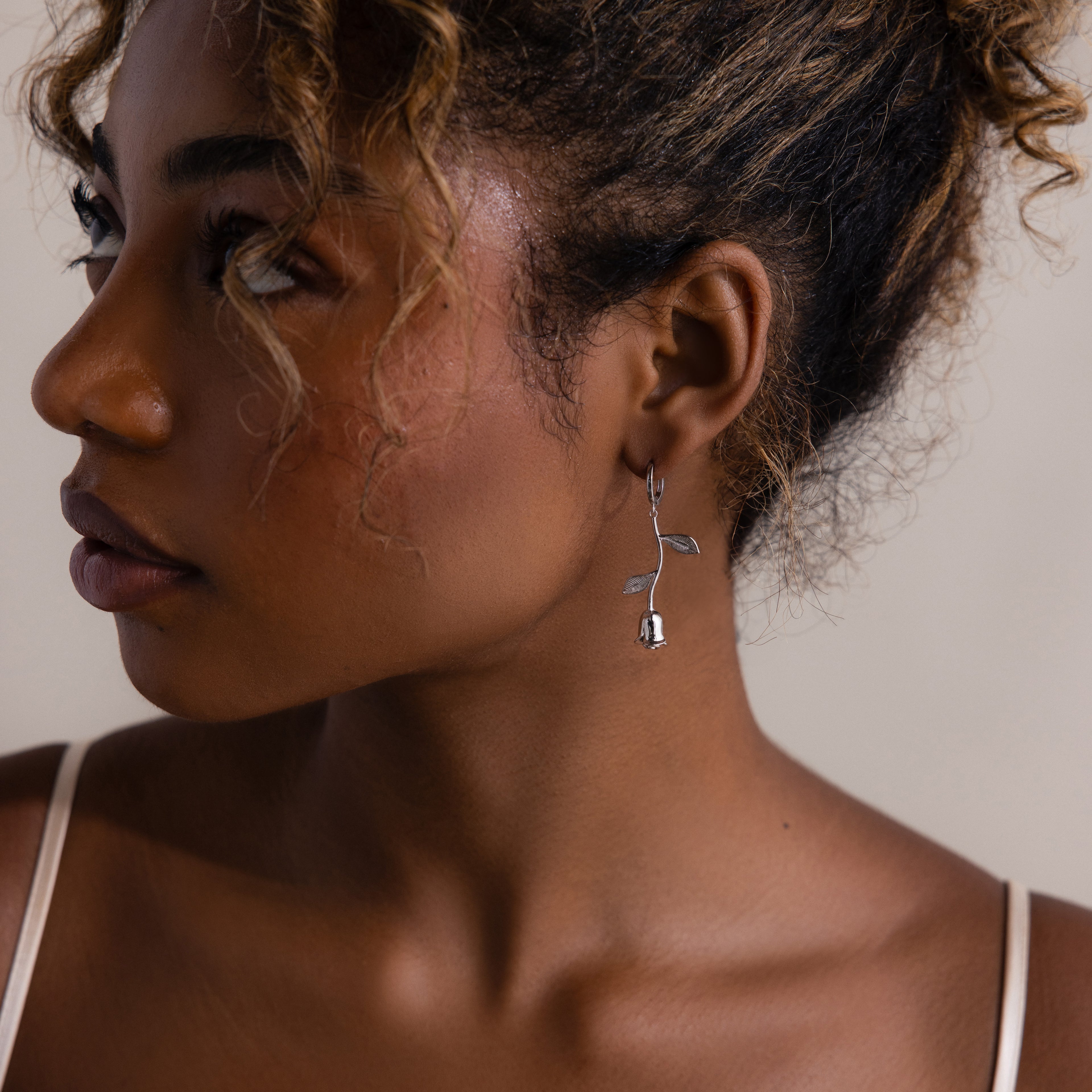 Close-up of a woman wearing a silver rose earring with a neutral background