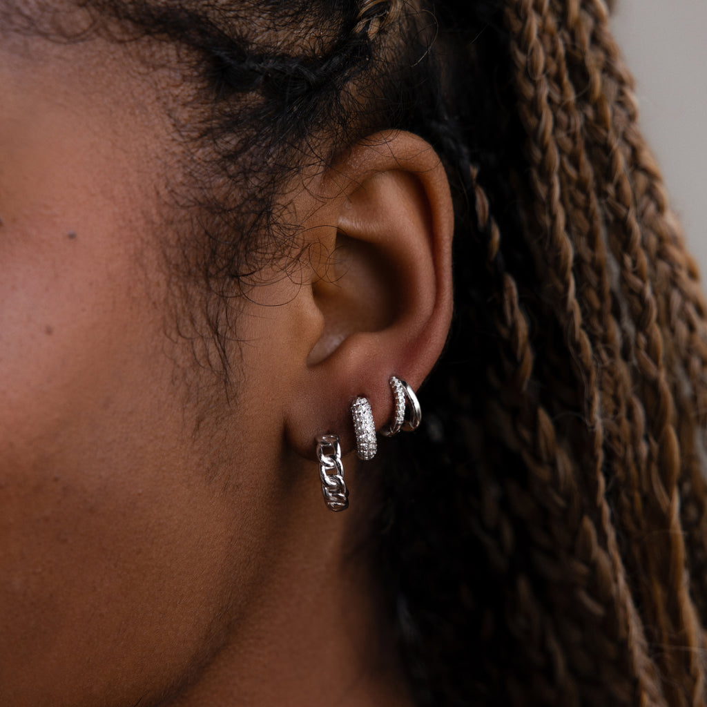 Close-up of an ear with three silver hoop earrings against a blurred background