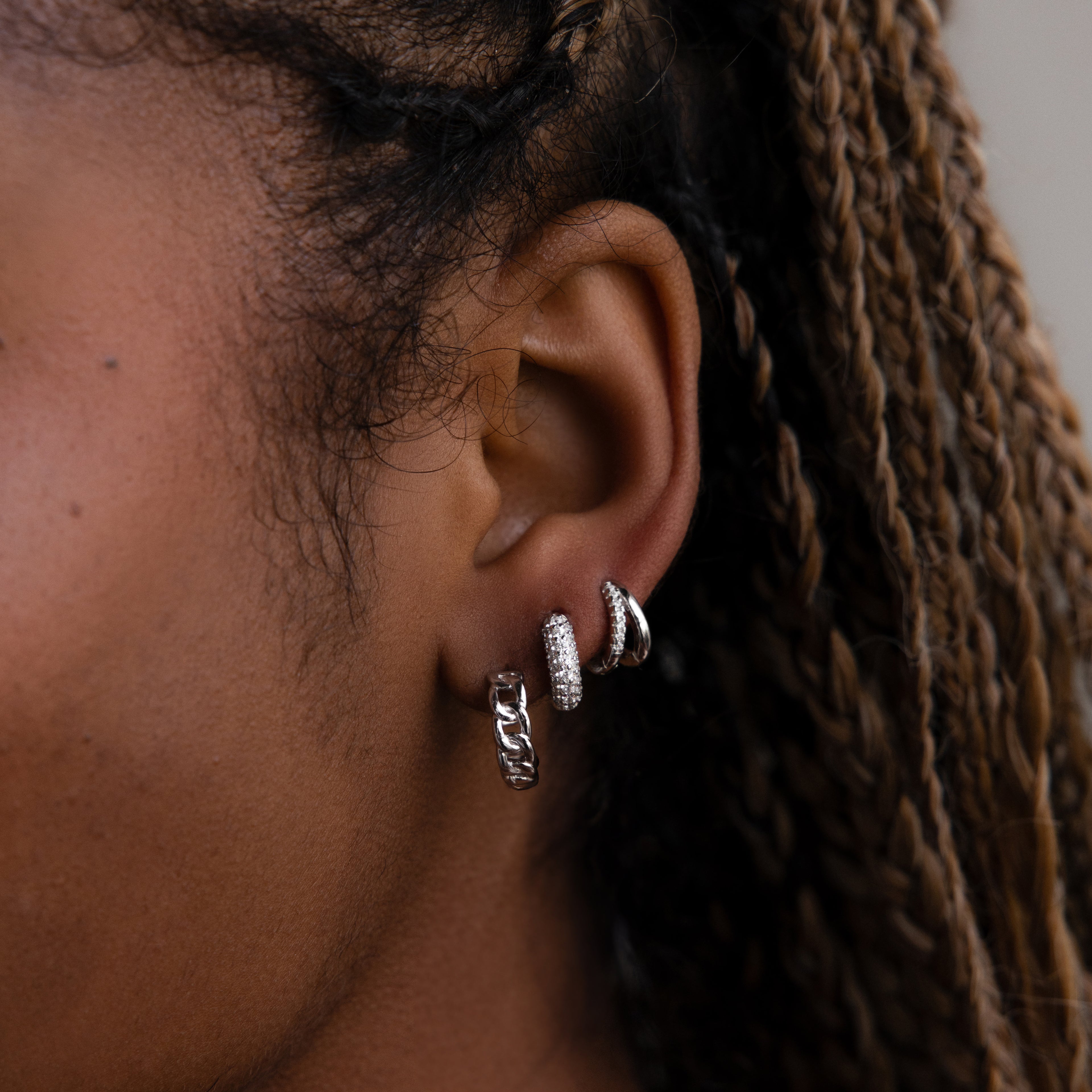 Close-up of an ear with three silver hoop earrings against a blurred background
