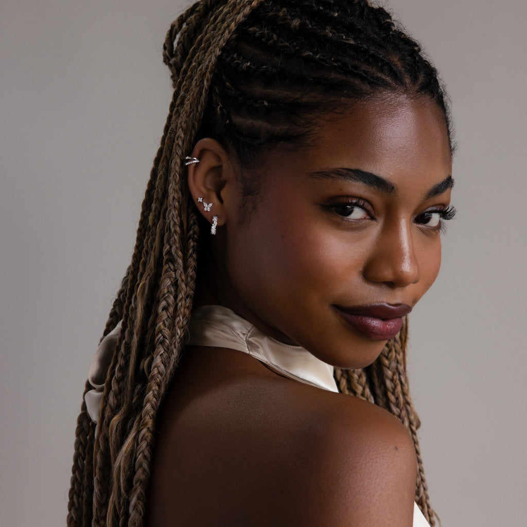 Woman with braided hair wearing silver diamond earrings against a neutral background