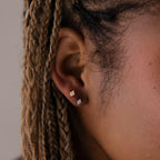Close-up of a model wearing two diamond stud earrings in gold and silver with braided hair.