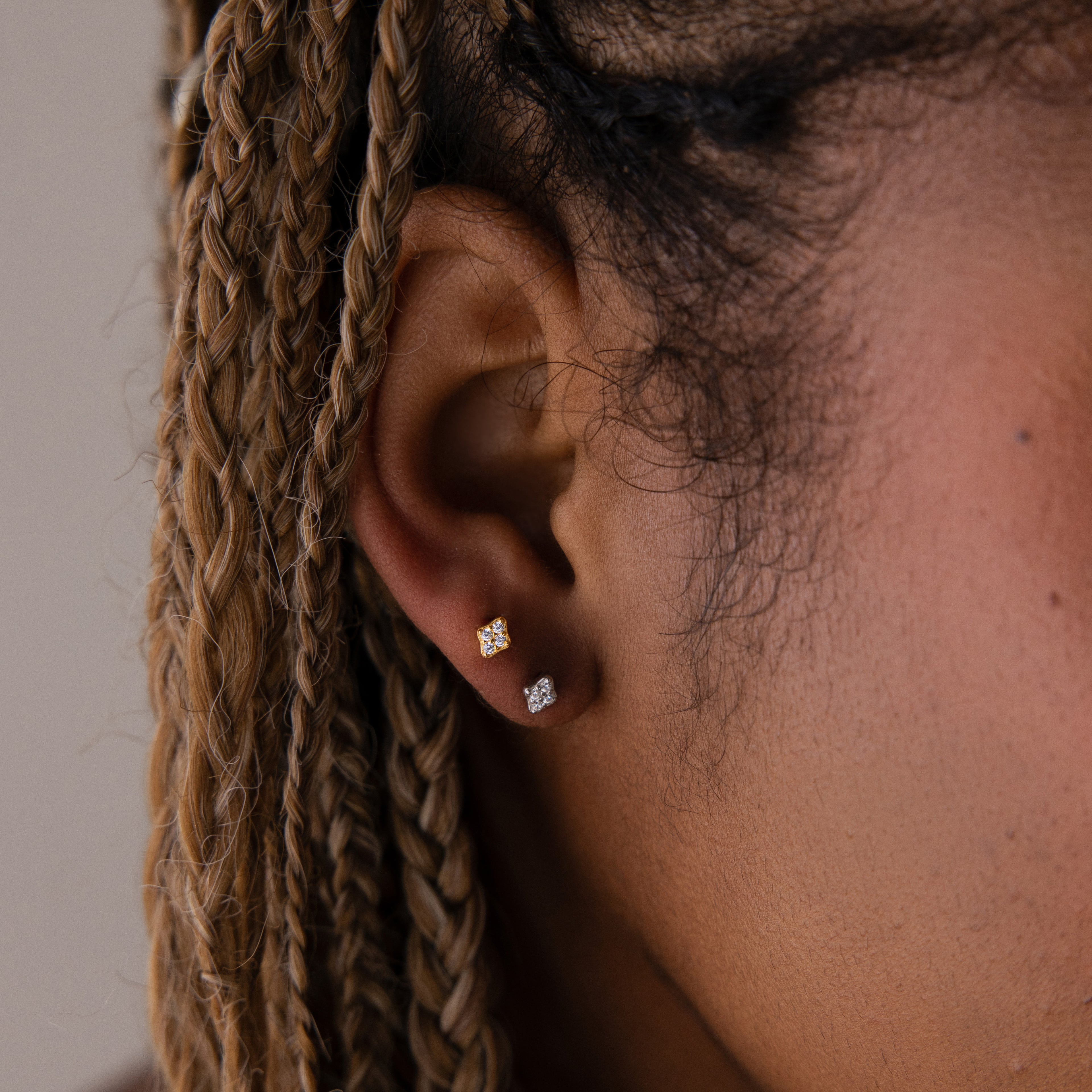 Close-up of a model wearing two diamond stud earrings in gold and silver with braided hair.