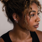 Close-up of a woman wearing multiple silver earrings with a neutral background