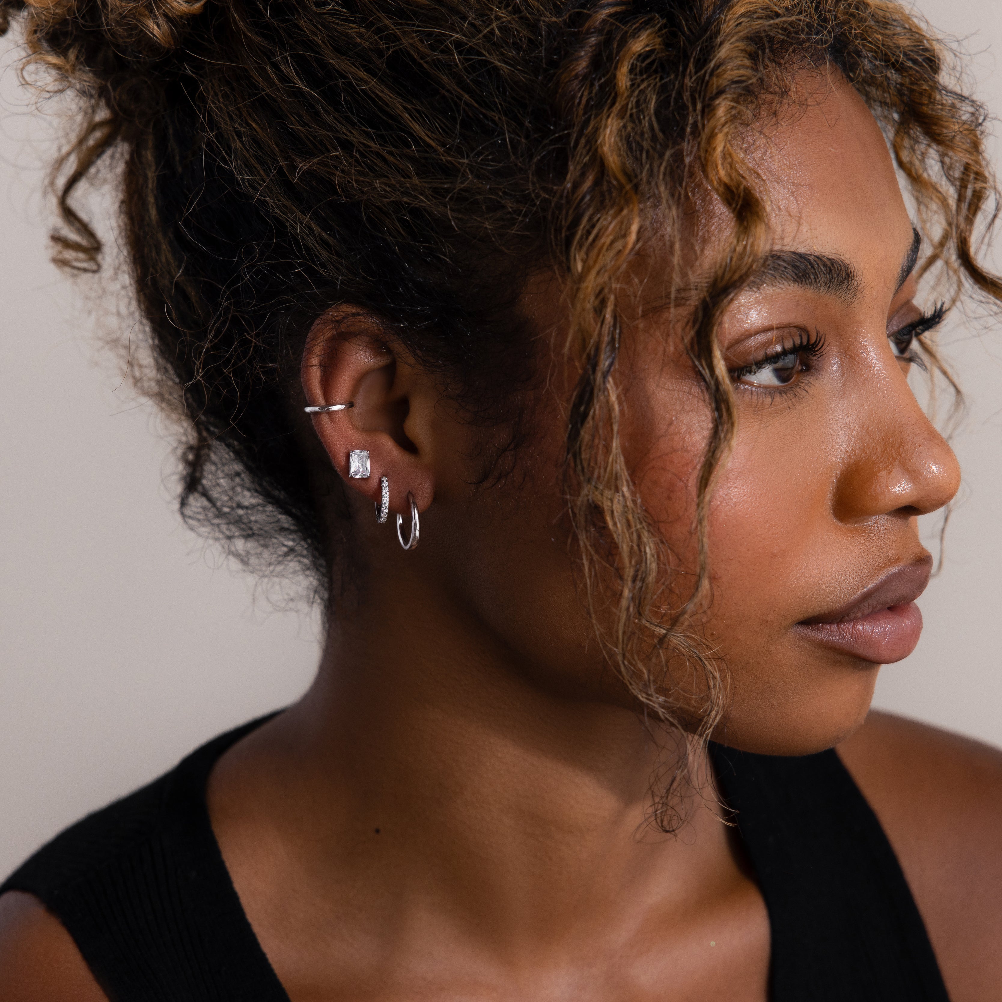Close-up of a woman wearing multiple silver earrings with a neutral background