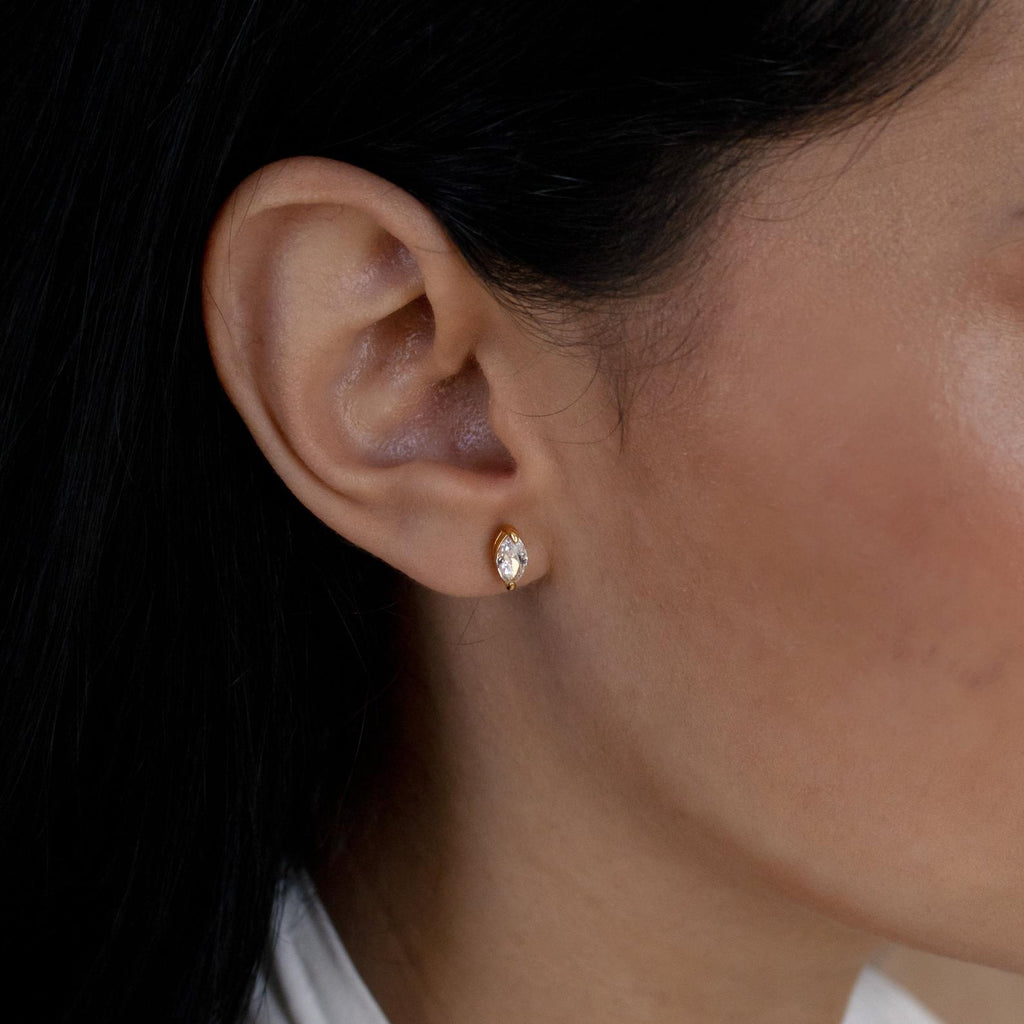 Close-up of a model wearing a gold marquise earring with a clear gemstone.