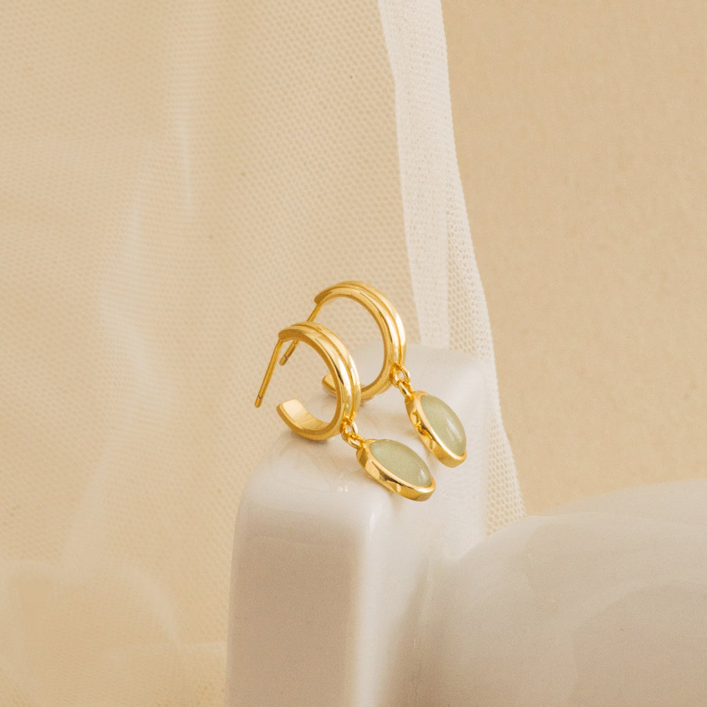 Gold stud hoop earrings with green jade gemstones on a beige background