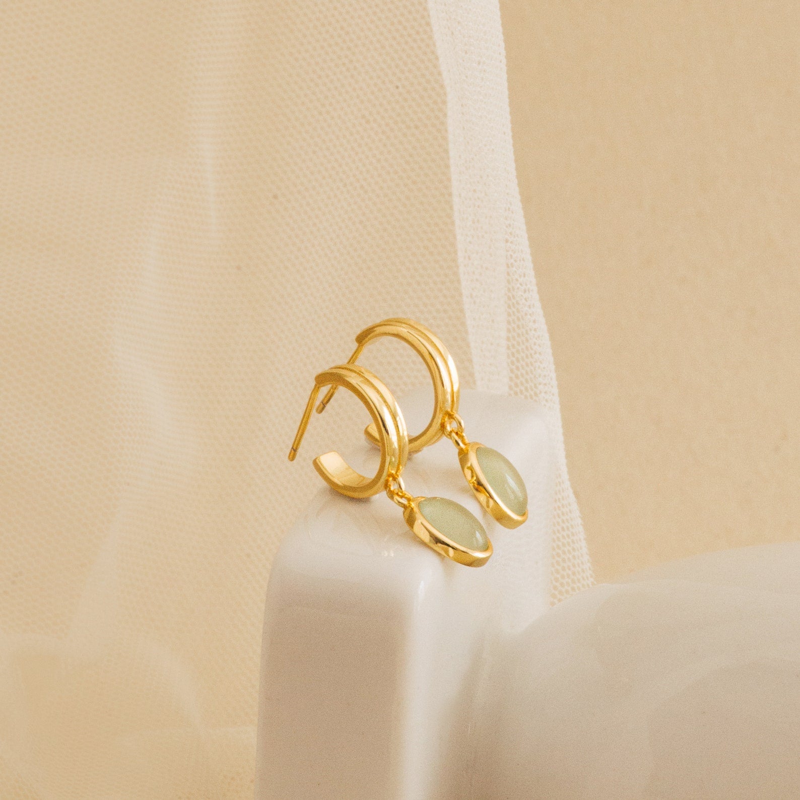 Gold stud hoop earrings with green jade gemstones on a beige background