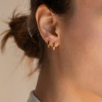 Close-up of a model wearing gold hoop earrings with a neutral background