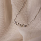 The Mrs. Necklace features a delicate script pendant, ideal as a wedding gift for any bride-to-be, showcased on a soft beige textured fabric background.