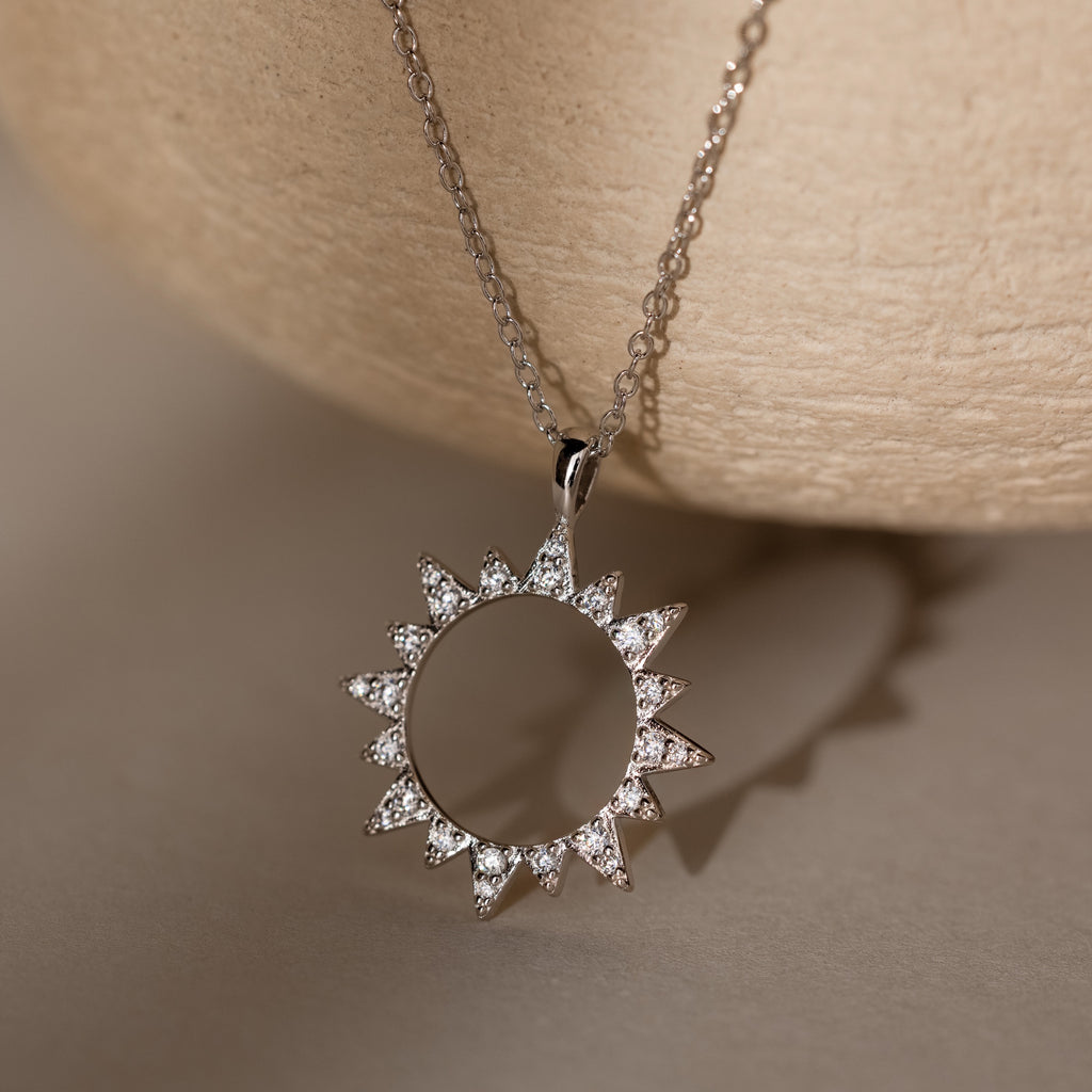 The Pave Sun Necklace features glittering pave accents and small diamonds, showcased against a neutral textured background.