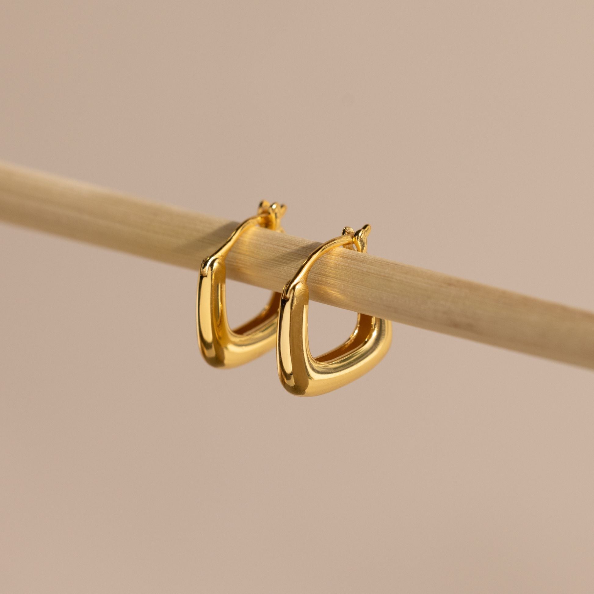 Close-up of gold geometric square hoop earrings hanging on a bamboo rod.