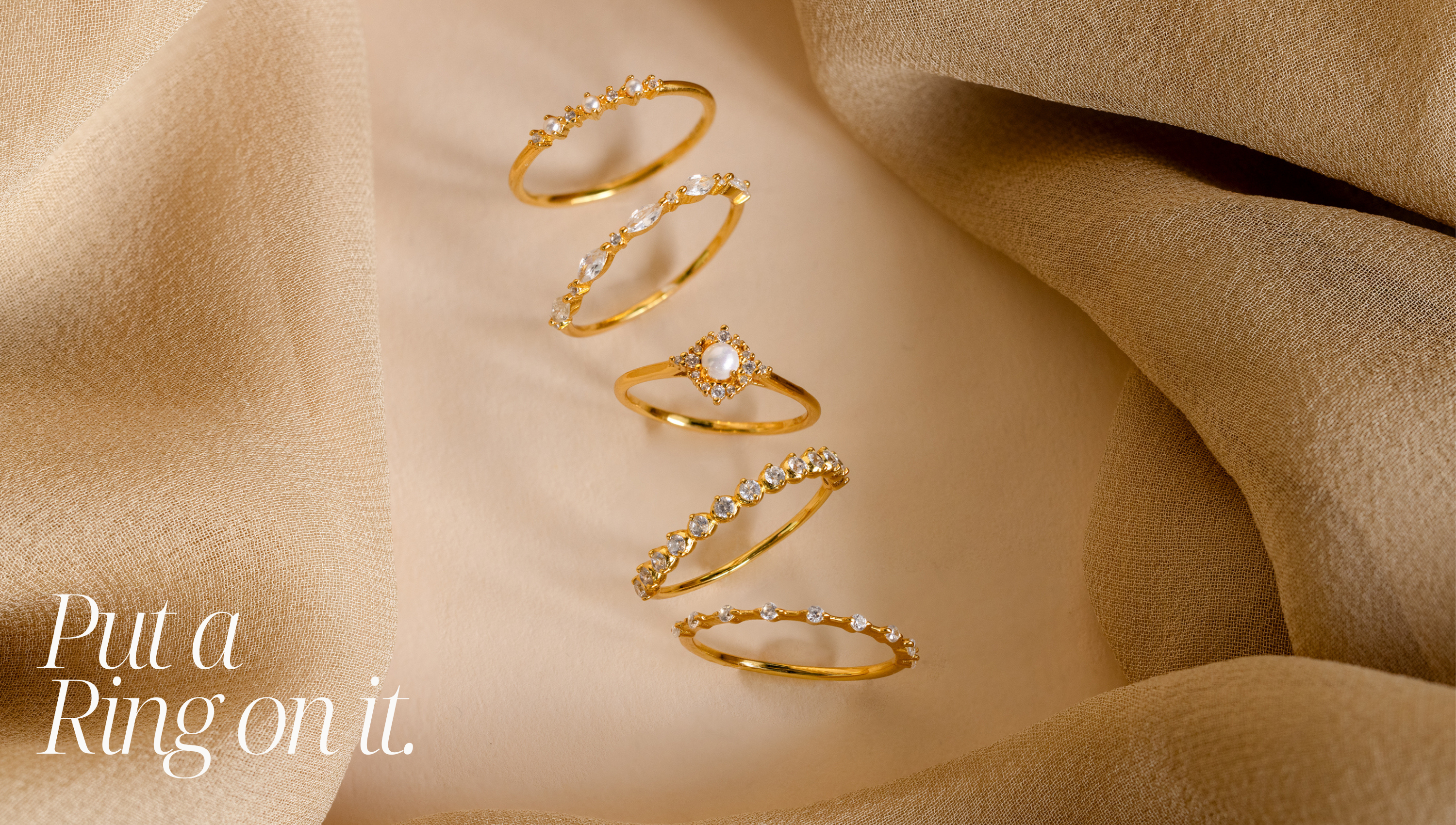 A horizontal jewelry flat lay photo featuring a row of 5 gold rings, the 1st and 3rd rings are both pearl diamond rings. The 2nd, 4th and 5th rings are all thin diamond rings. In the bottom left corner contains the text "put a ring on it".