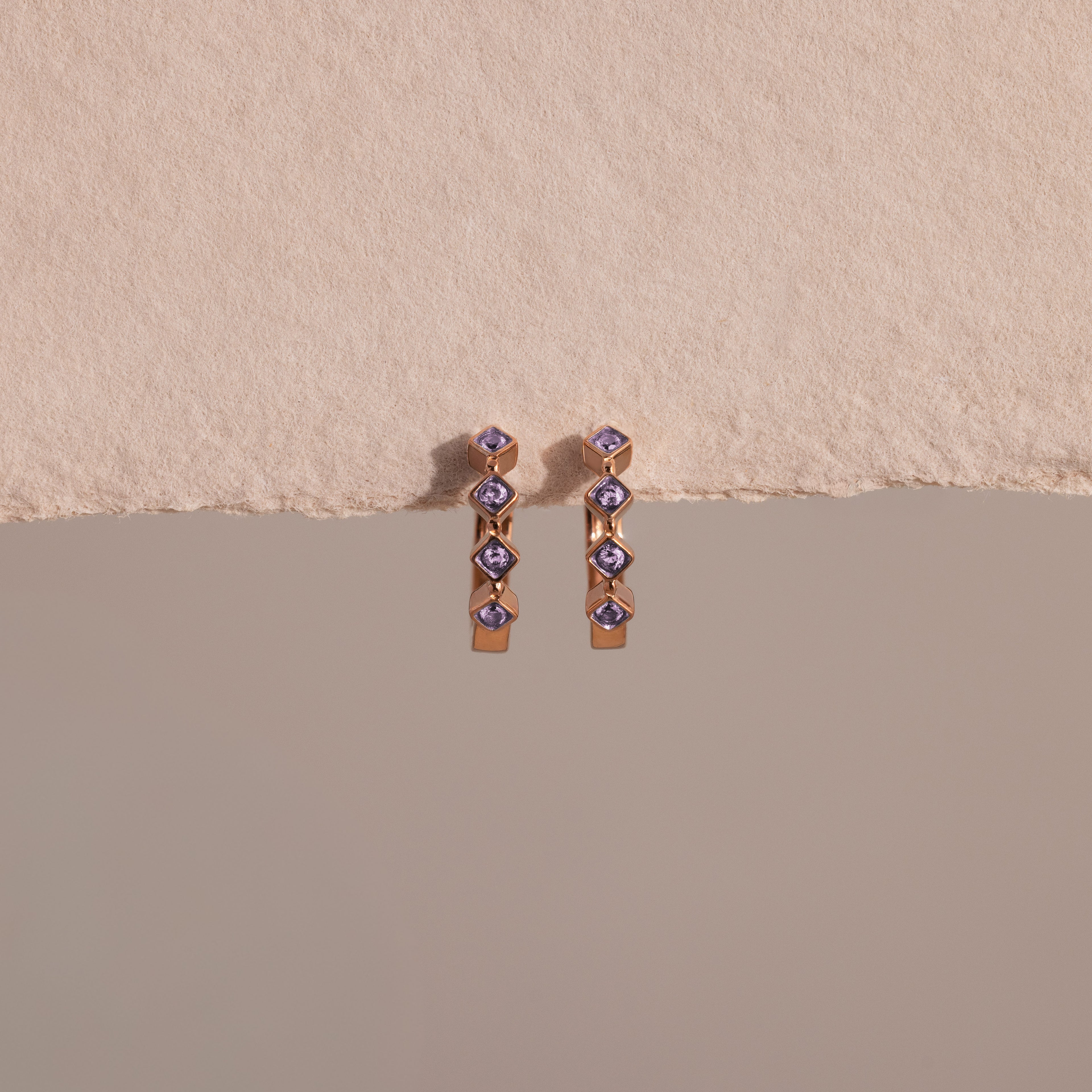 The Geometric Alexandrite Huggies are earrings with blue alexandrite stones, featuring a geometric design and subtle diamond accents for added sparkle.