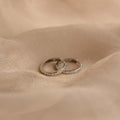 Two slim silver Classic Diamond Sprinkle Huggies with small clear stones set along the front, resting on draped beige fabric.