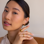 A woman with smooth skin wears the Pave Triple Spike Huggies, her minimalist gold and diamond earrings adding modern elegance as she gazes softly at the camera.