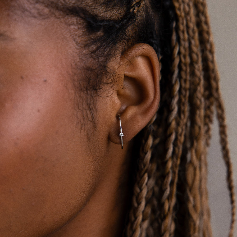 Close-up of a woman with a small hoop stud earring, hair styled in braids.