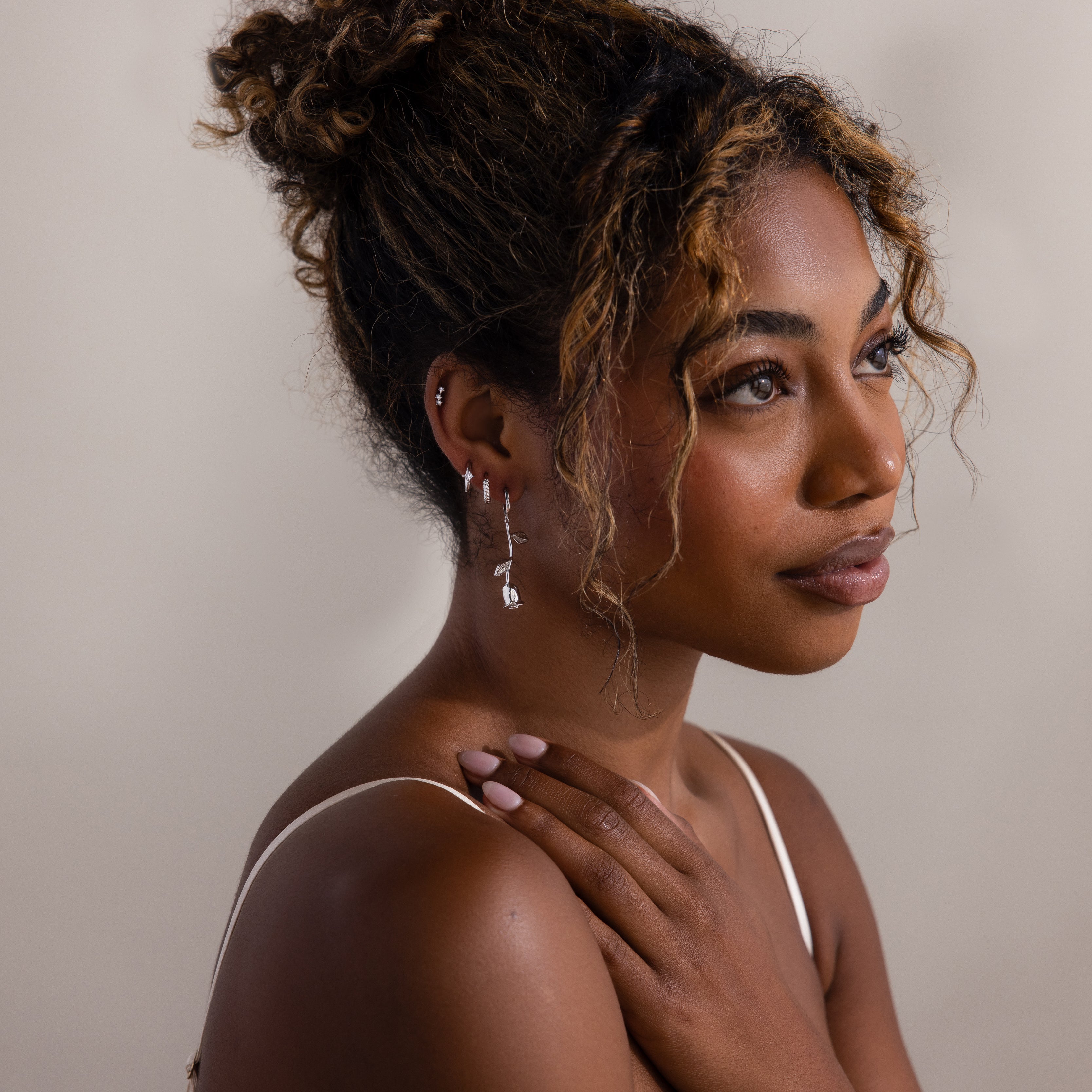 Woman with styled hair and silver earrings against a neutral background