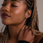 Close-up of a woman with braided hair and a silver bar stud earring touching her neck against a neutral background
