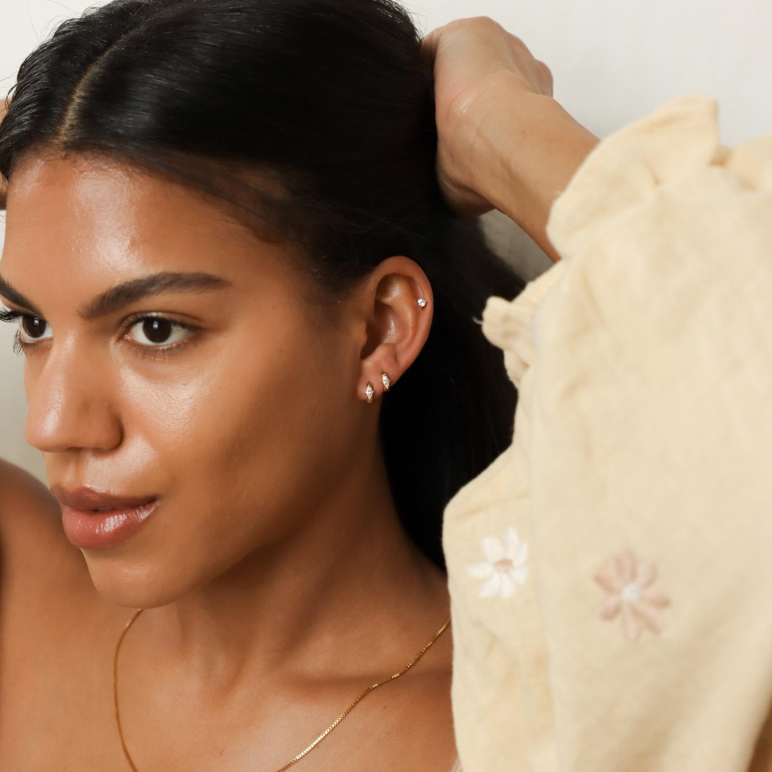 Woman adjusting her hair wearing various marquise shaped earrings in a neutral background