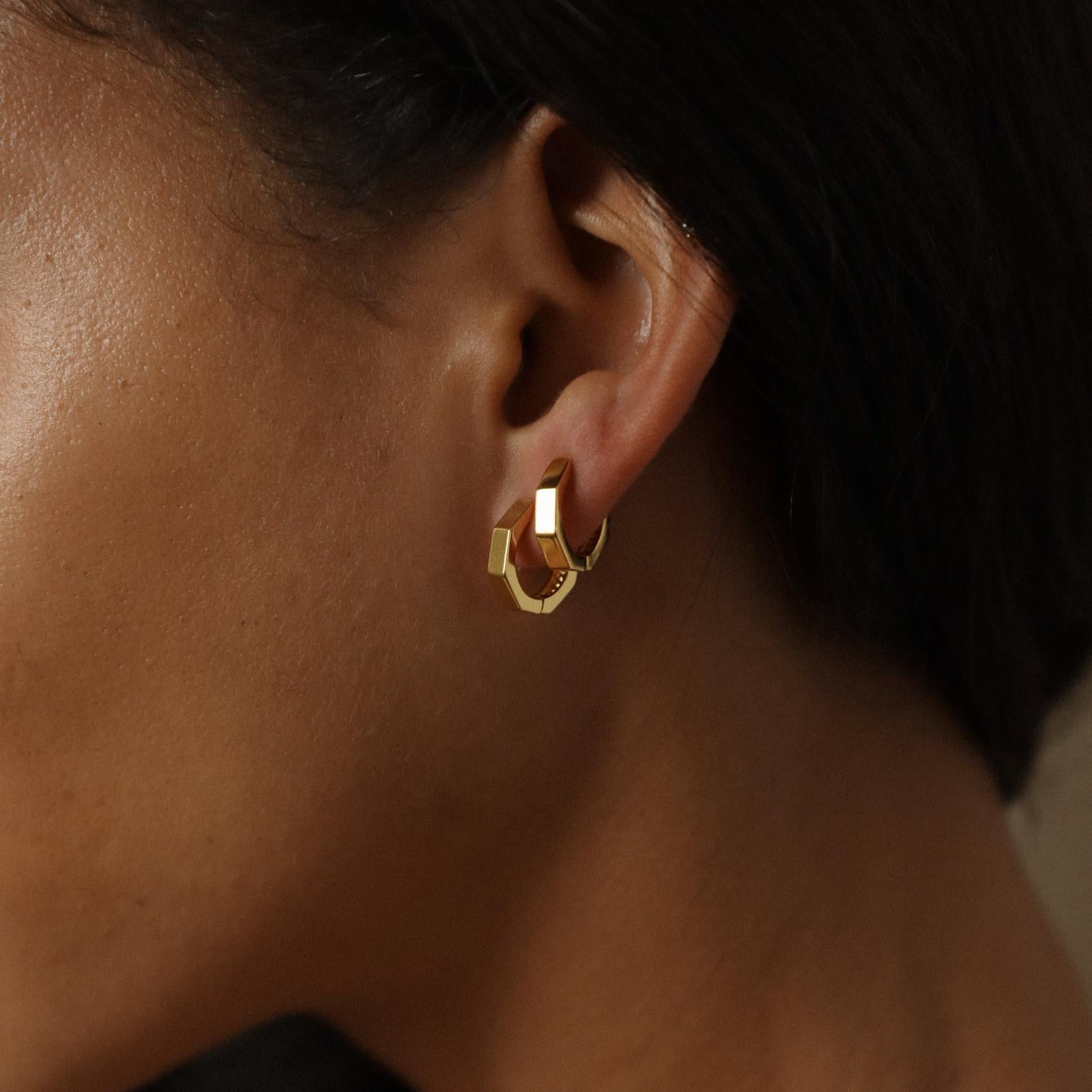 Close-up of a model wearing gold hoop earrings with a dark background