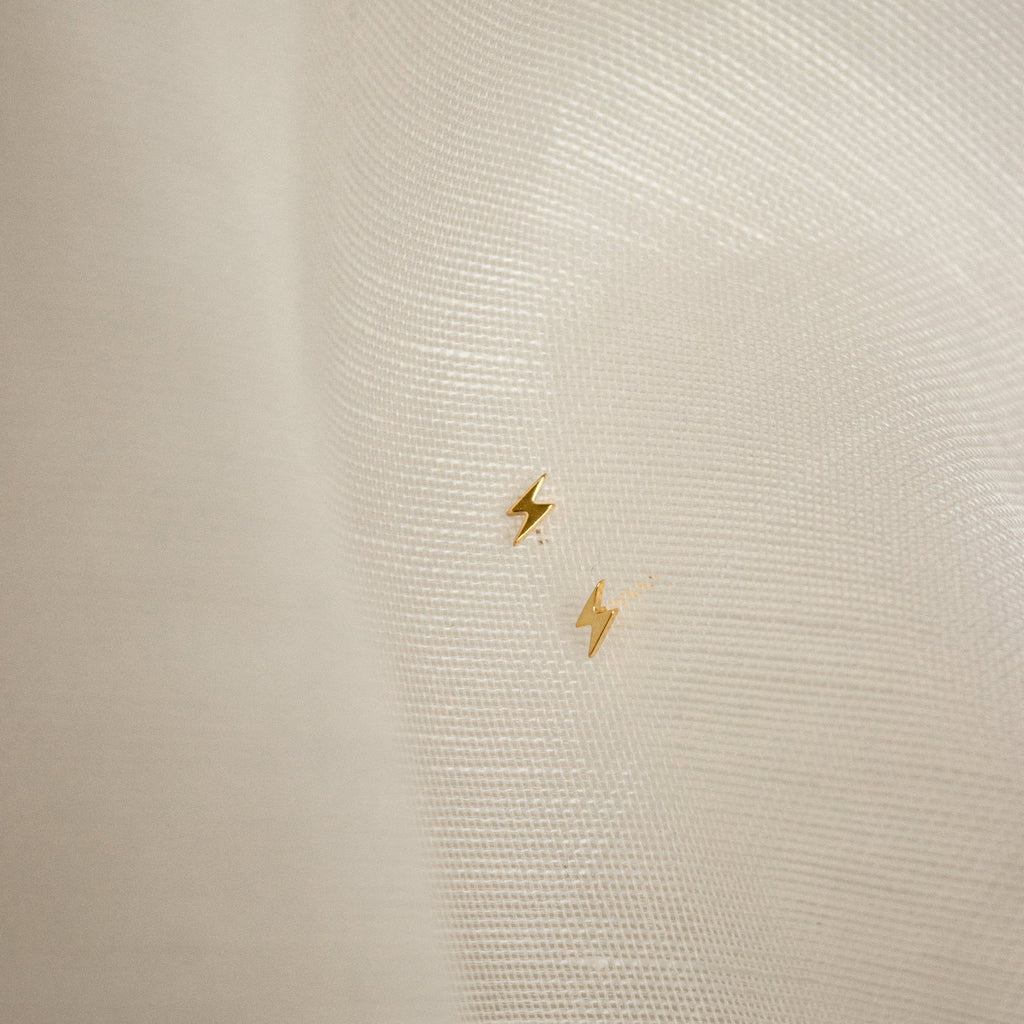 Gold lightning bolt earrings on a textured beige background