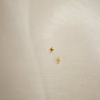 Gold lightning bolt earrings on a textured beige background