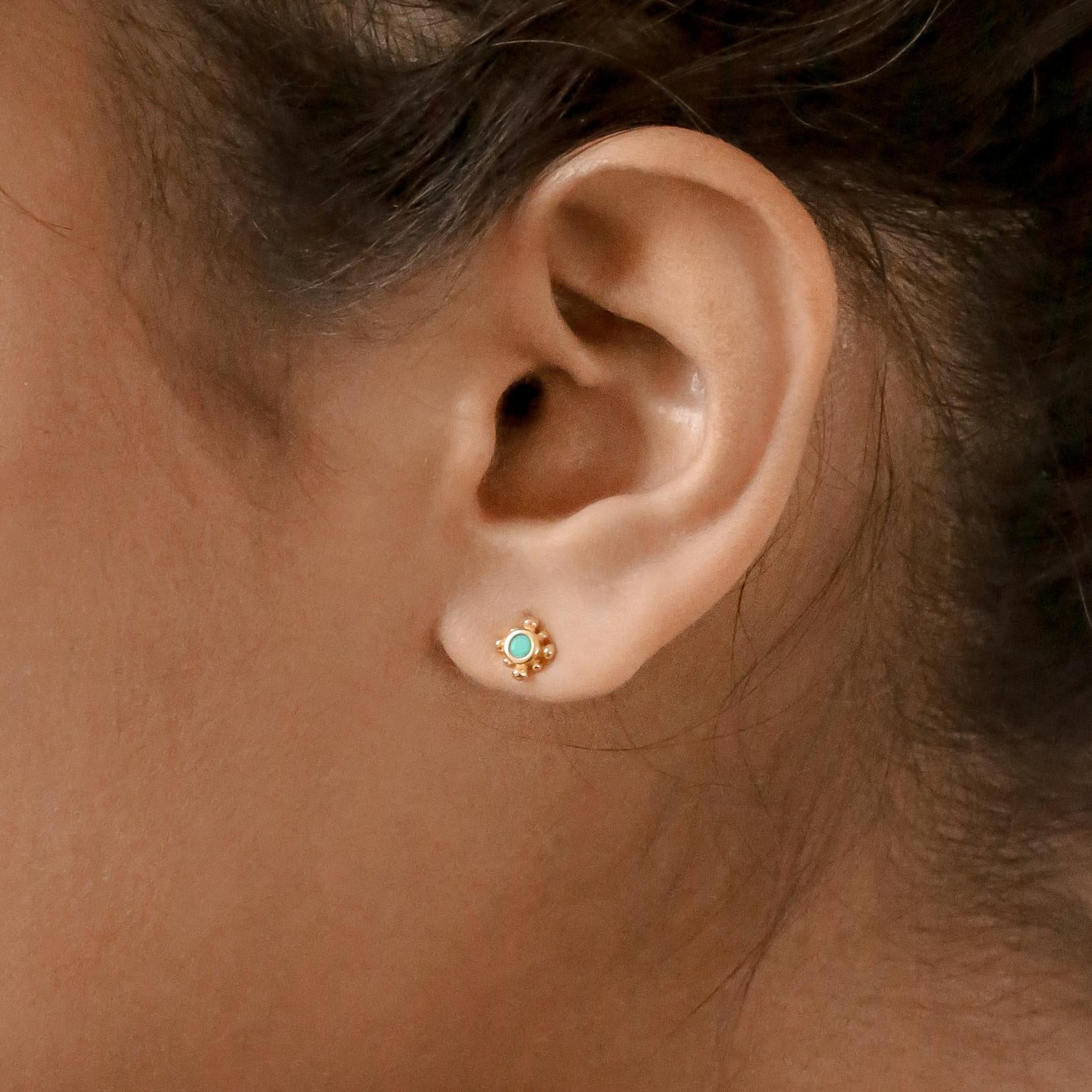 Close-up of a model wearing a gold earring with a turquoise gemstone.