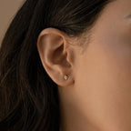 Close-up of a model wearing a gold diamond stud earring with dark hair and a beige background