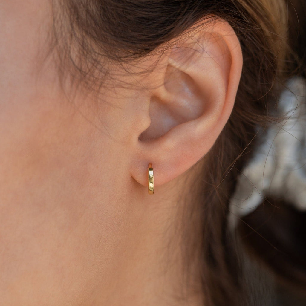 Close-up of a model wearing a dainty gold hoop earring with blurred background