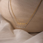 A gold and a silver script Mrs. necklace rest on a white textured surface—an ideal gift for the bride-to-be before she officially becomes a Mrs.