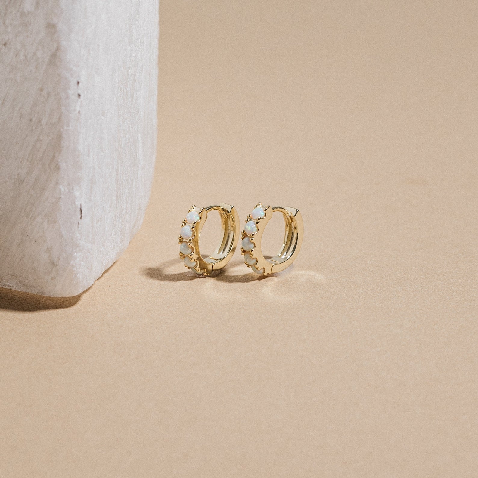 Gold hoop earrings with opal stones on a beige surface